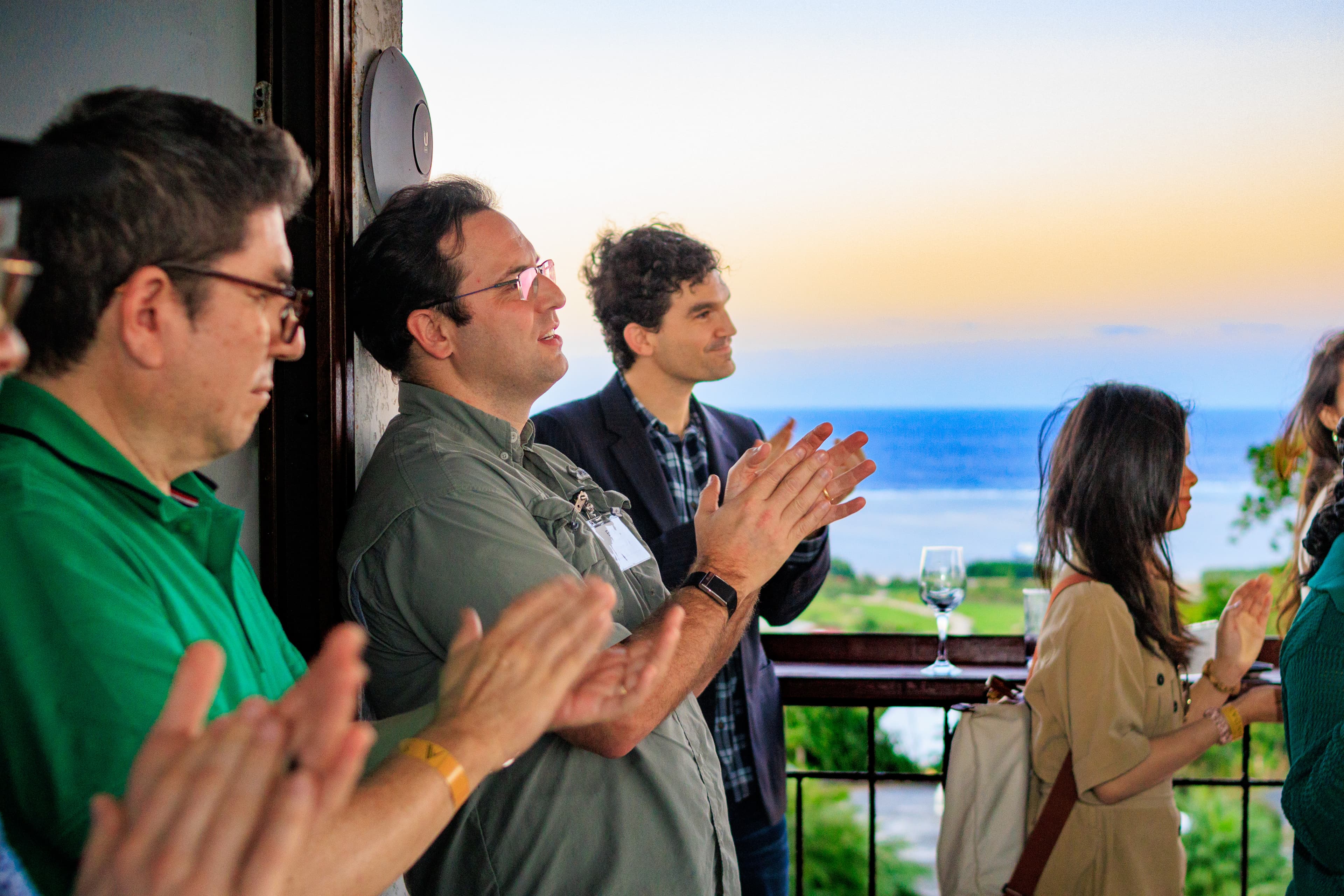 People applauding at a Próspera event with a beautiful ocean sunset view in the background.