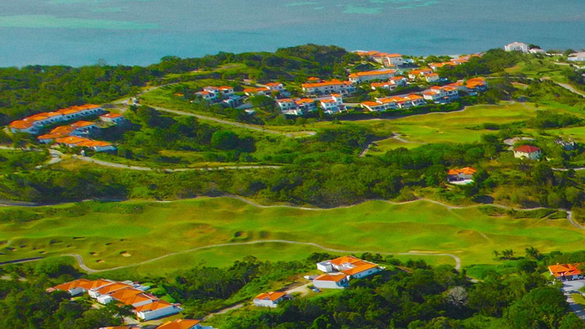 Elegante sala de estar costera con vista panorámica al océano a través de grandes puertas corredizas de vidrio. Cuenta con un espacioso sofá seccional gris con cojines estampados en azul y blanco, mesa de café de madera y pisos de baldosas pulidas. Diseño interior luminoso y aireado perfecto para casas de lujo frente al mar o alquileres vacacionales de alta gama.